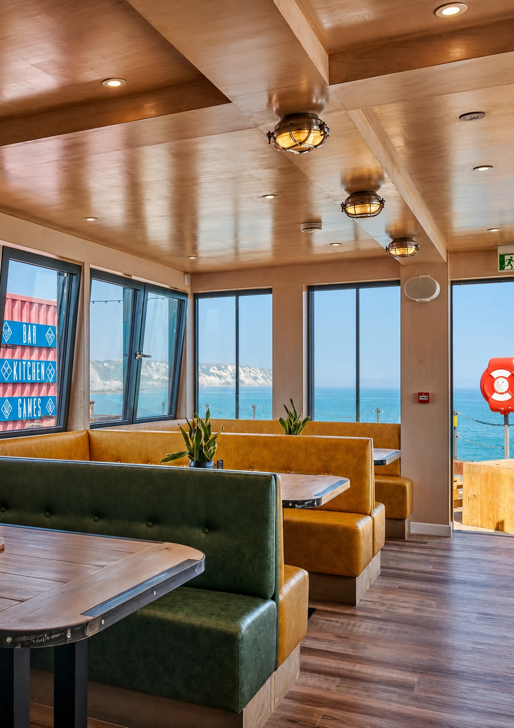 Olive-green and yellow booth seating inside Sailbox with Folkestone Harbour beyond